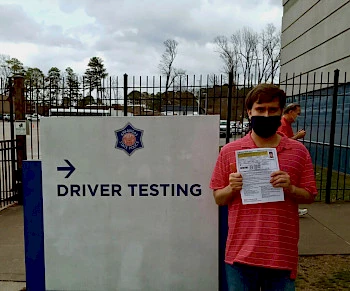 teenage boy standing next to a Driver Testing sign holding a piece of paper