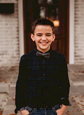 Young boy in a bow tie standing in front of a building and smiling