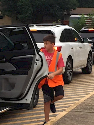 school-aged boy in an orange safety vest opens a car door